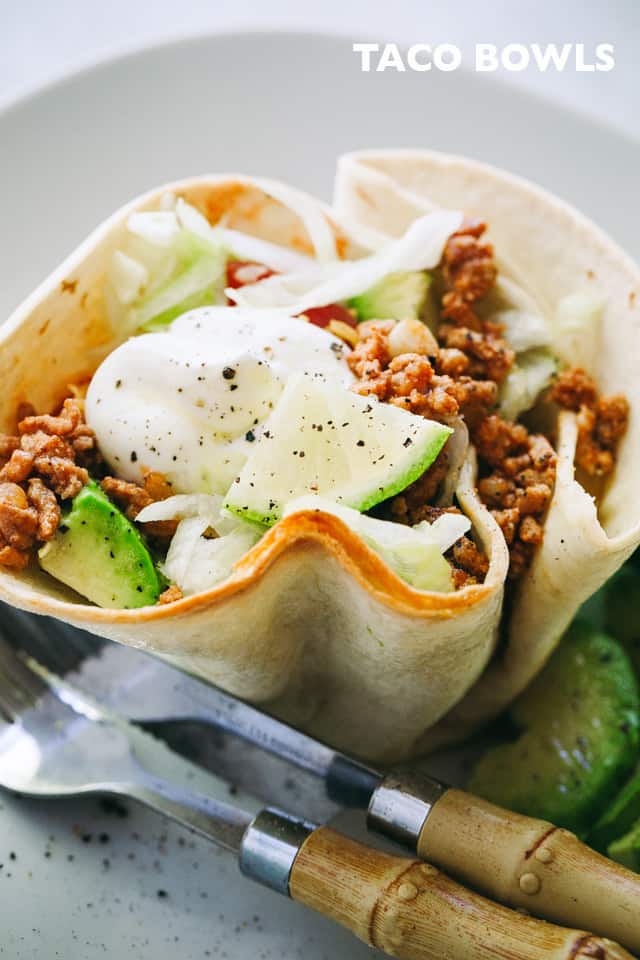 Taco Bowls filled with taco-seasoned ground turkey meat, salad, tomatoes, cheese, and topped with a dollop of sour cream
