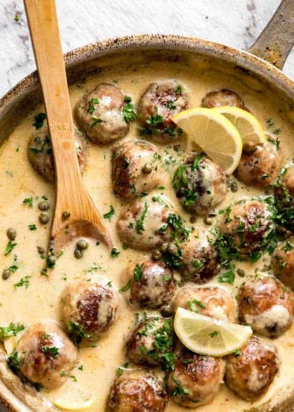 Creamy Lemon Chicken Piccata Meatballs in a skillet with fresh herbs and lemon wedges