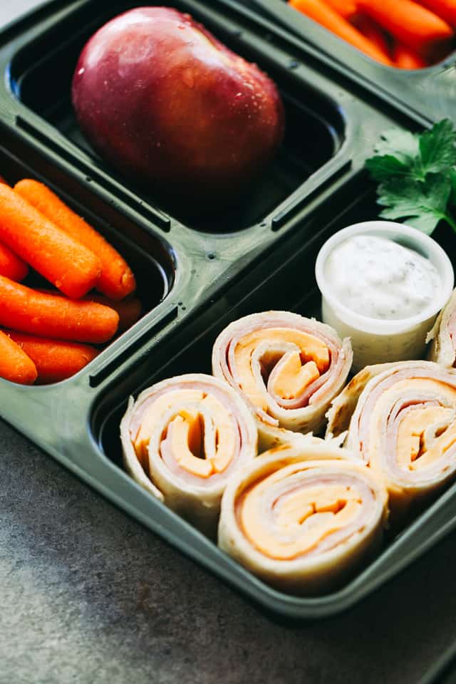 Ham and Cheese Pinwheels in a lunch box with carrots and an apple.