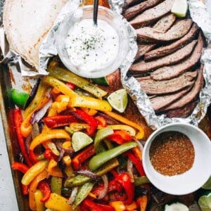 Sheet pan steak fajitas with lime wedges, tortillas, and plain yogurt for serving.