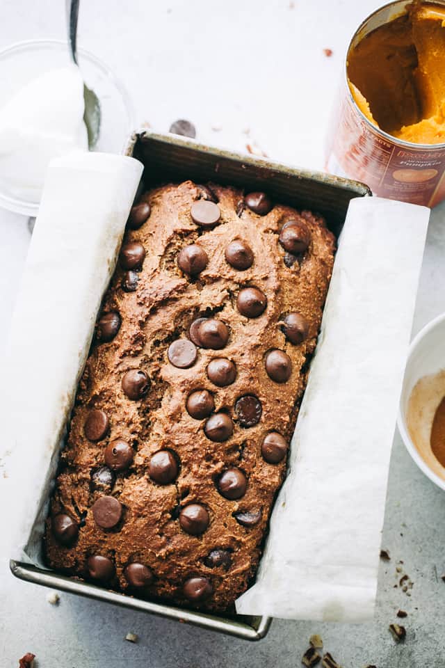 A loaf of bread packed with pumpkin and chocolate chips freshly baked in a pan lined with parchment paper