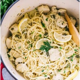 Chicken piccata pasta in a pot beside a lemon and a sprig of fresh parsley