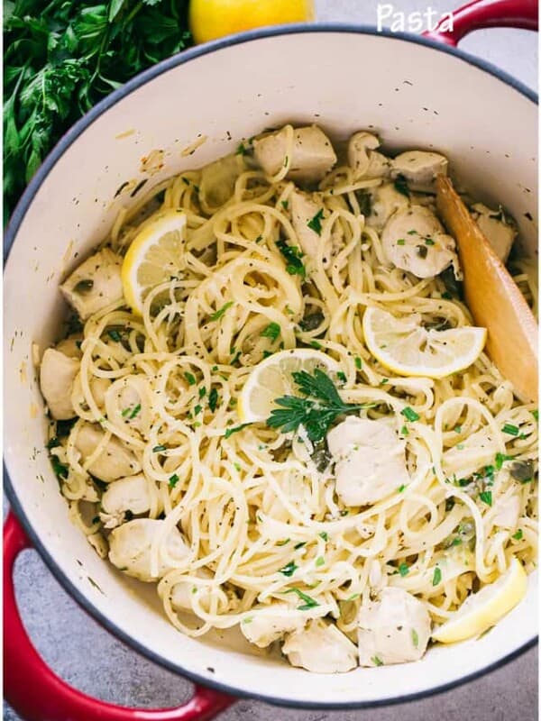 Chicken piccata pasta in a pot beside a lemon and a sprig of fresh parsley