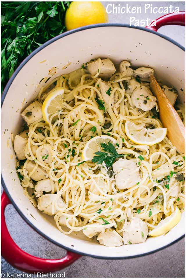 Chicken piccata pasta in a pot beside a lemon and a sprig of fresh parsley