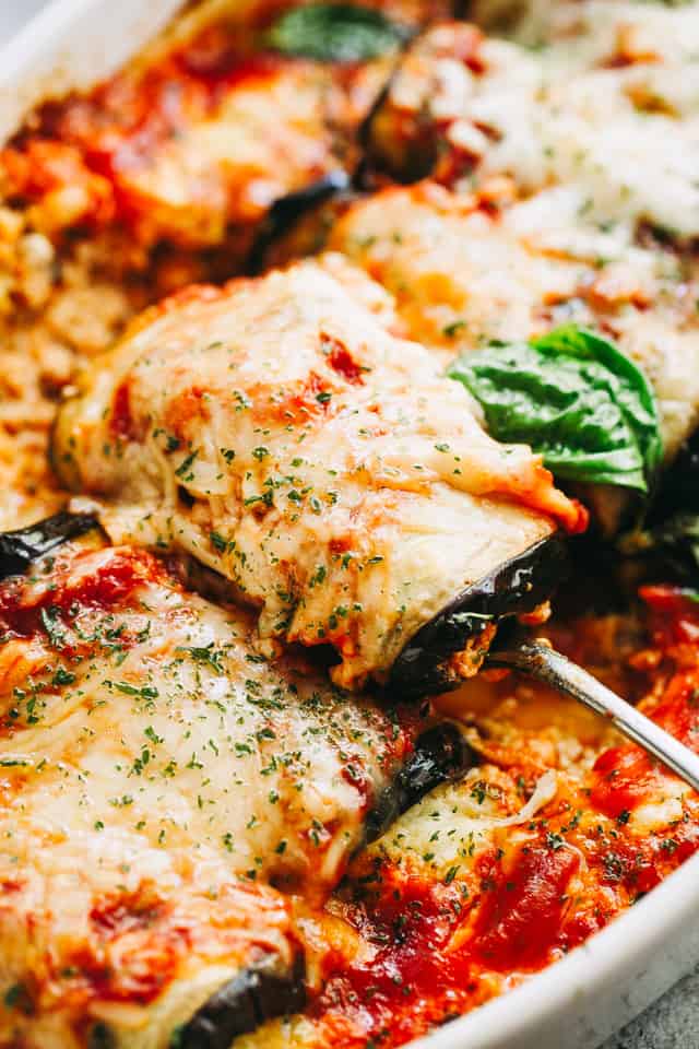 A close-up of a spoon pulling up eggplant rollatini from a baking dish.