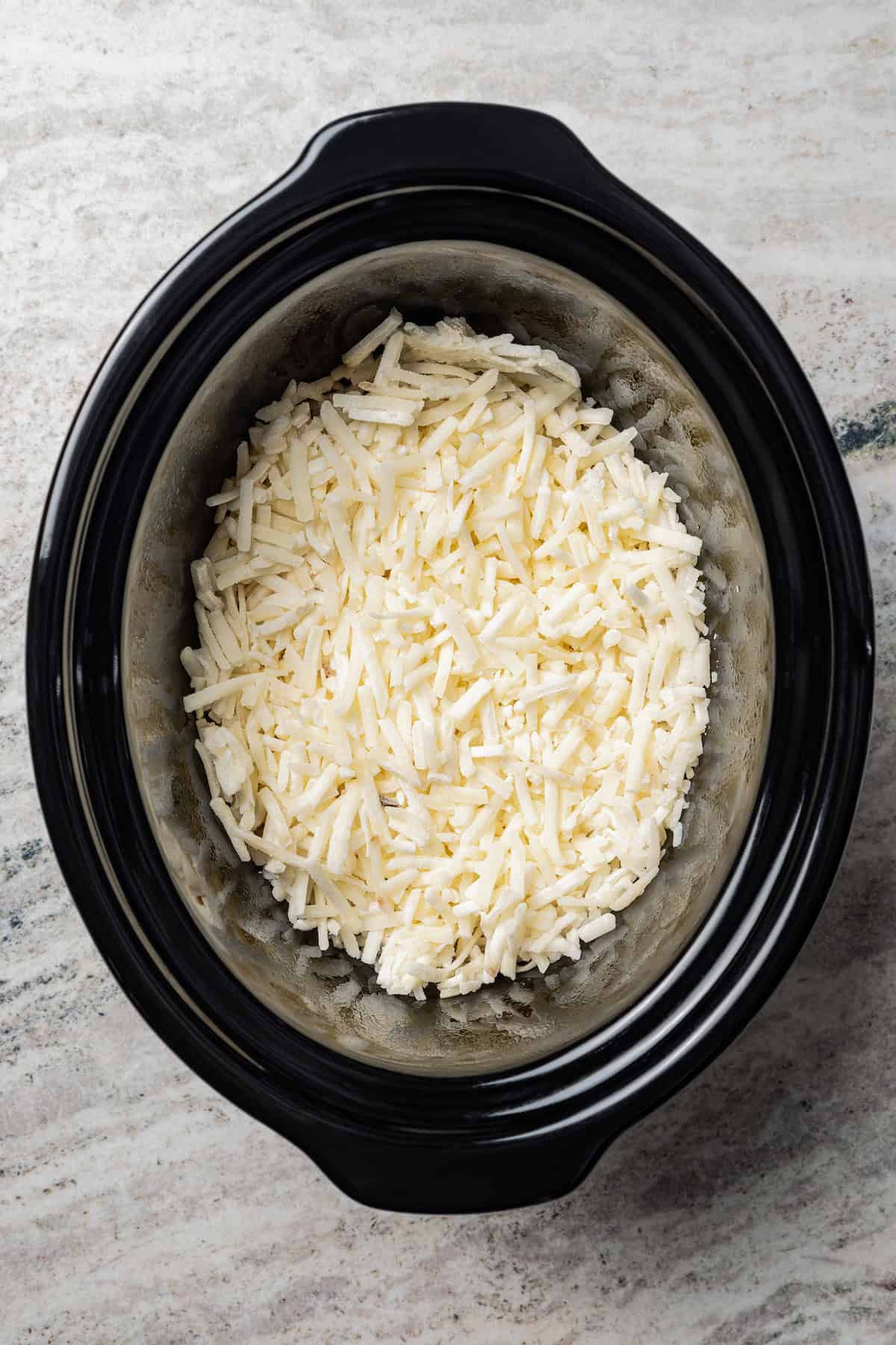 Shredded potatoes in the bottom of the slow cooker.