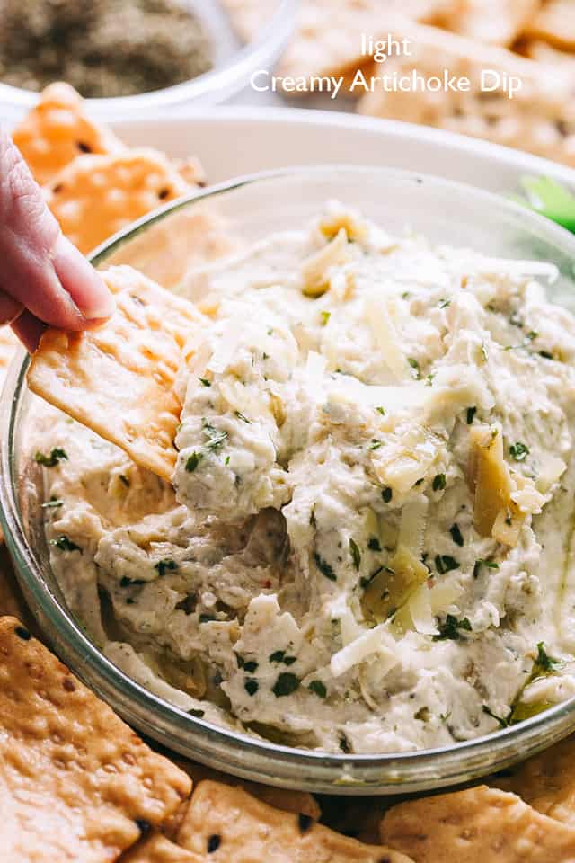 Creamy artichoke dip is scooped up on a cracker.