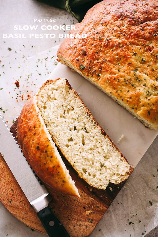 Overhead shot of sliced slow cooker bread on a cutting board with a bread knife set next to the bread slices.