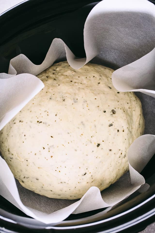 Bread dough set inside a slow cooker lined with parchment paper.