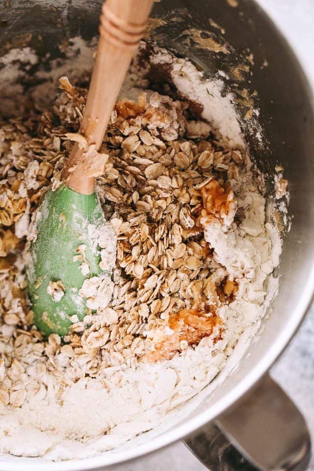 Apple oatmeal cookie dough coming together in a metal mixing bowl with a spatula.