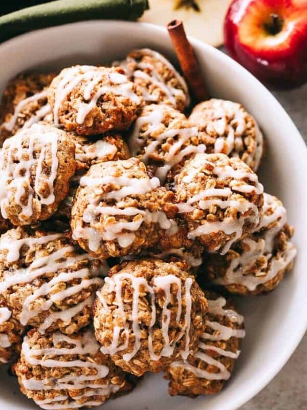 Overhead view of apple oatmeal cookies piled in a large white bowl garnished with cinnamon sticks.