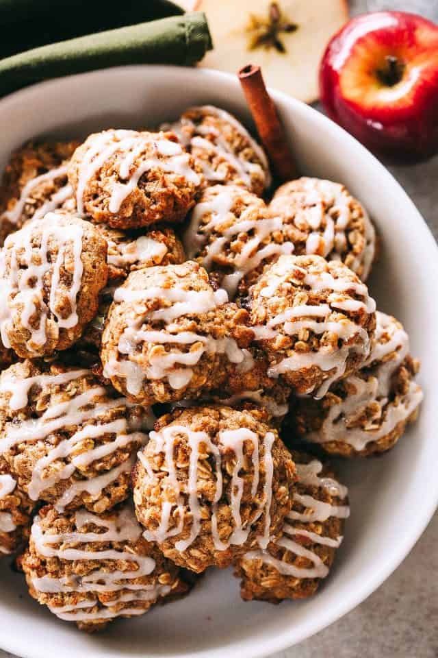 Overhead view of apple oatmeal cookies piled in a large white bowl garnished with cinnamon sticks.