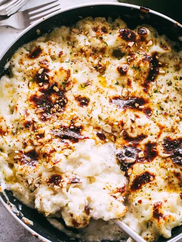 Overhead view of cauliflower gratin in a skillet with a spoon for serving.