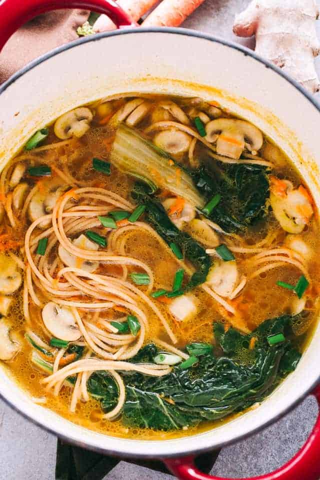 A pot of soup with noodles, swiss chard, and mushrooms.