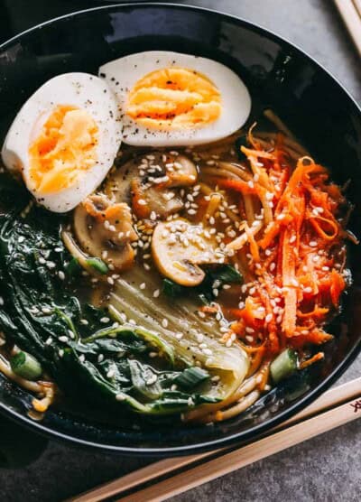 Overhead image of a black bowl filled with soup, soba noodles, mushrooms, and hard-boiled eggs.