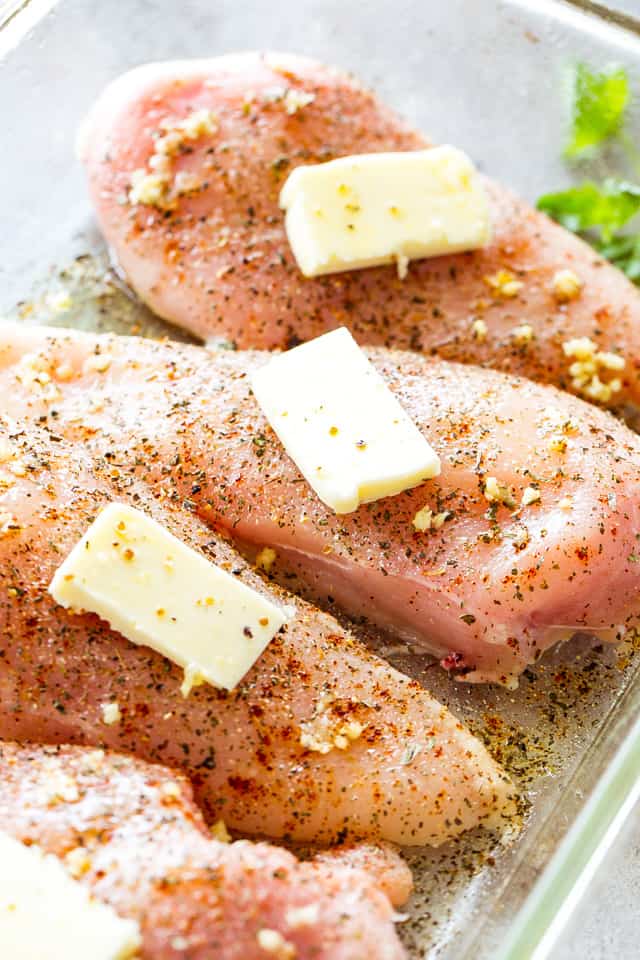 Raw chicken in a baking dish with pats of butter on top of each chicken breast.