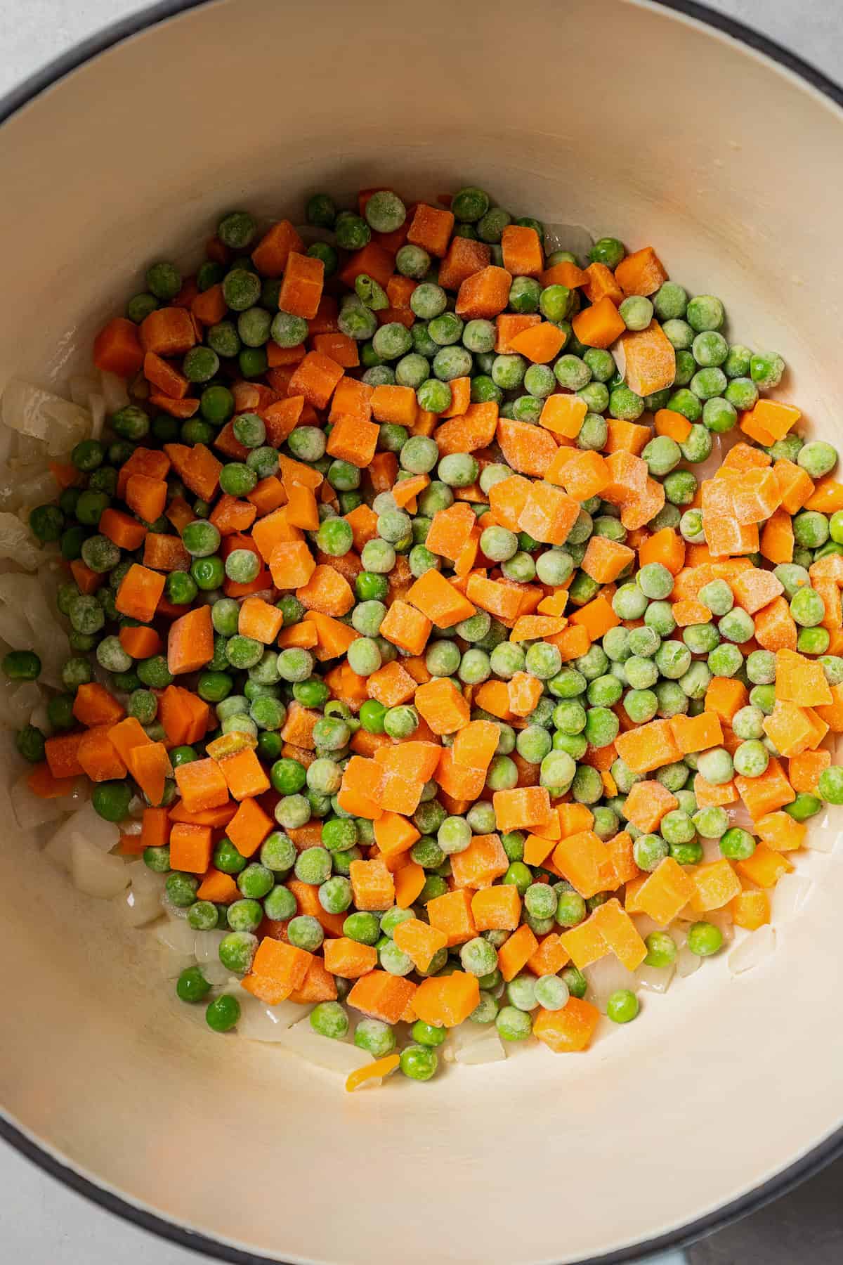 Frozen carrots and peas added to a large pot with onions.