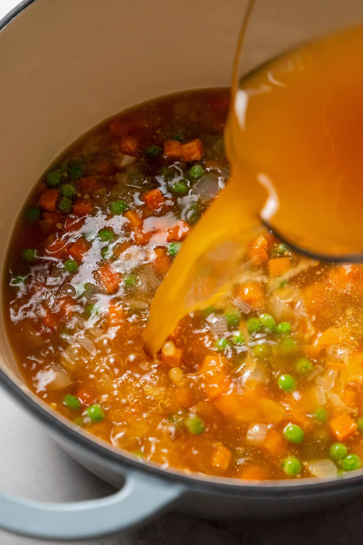 Broth being poured into a pot with veggies.