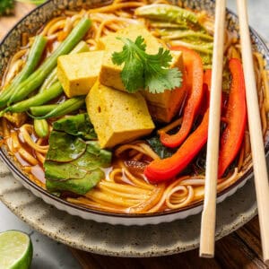 A bowl of noodles and broth topped with Chinese hot pot ingredients, with a set of chopsticks resting on the edge of the bowl.