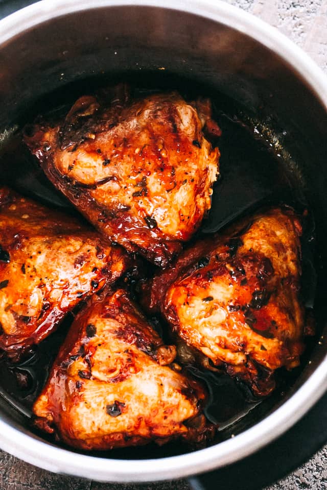 Four chicken thighs are arranged inside the insert of an instant pot.