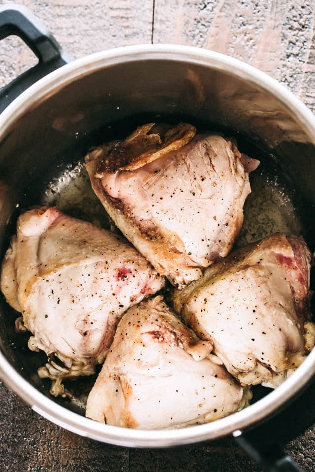 Four raw bone-in chicken thighs arranged inside a pot.