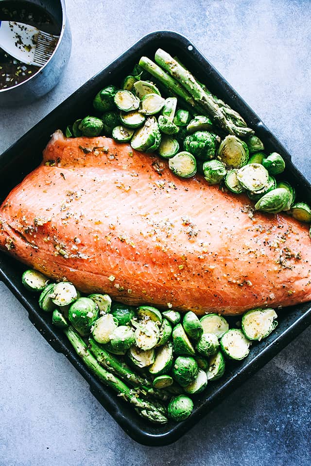 Seasoned salmon fillet surrounded by brussels sprouts and asparagus.