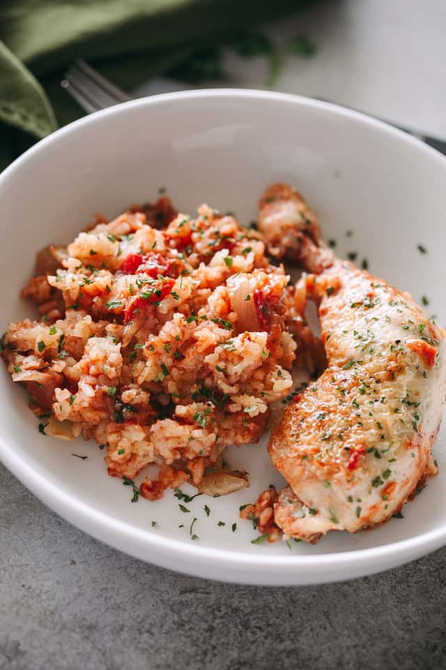 A browned and slow-cooked chicken thigh in a shallow bowl with Crock Pot tomato rice