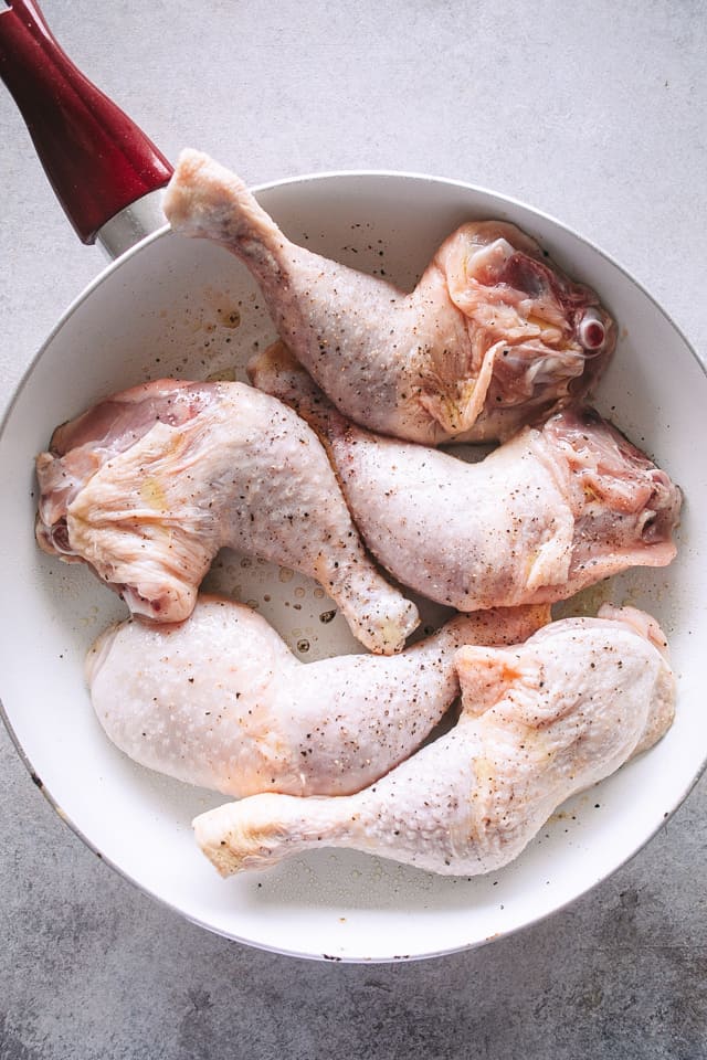 Five raw, seasoned chicken legs inside of a red and white saucepan