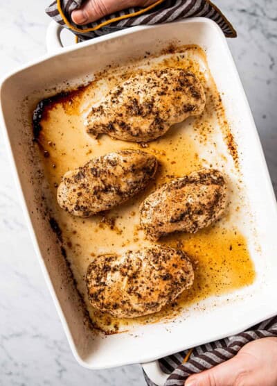 Hands holding baked chicken breasts in baking dish
