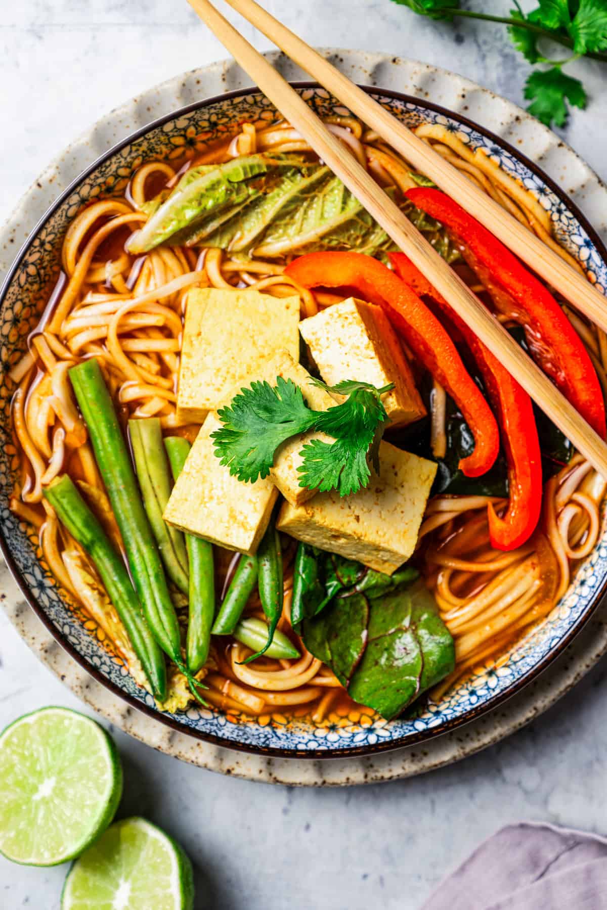 Overhead view of a bowl of noodles and broth topped with Chinese hot pot ingredients, with a set of chopsticks resting on the edge of the bowl.