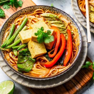 Overhead view of a bowl of noodles and broth topped with Chinese hot pot ingredients on a wooden board.