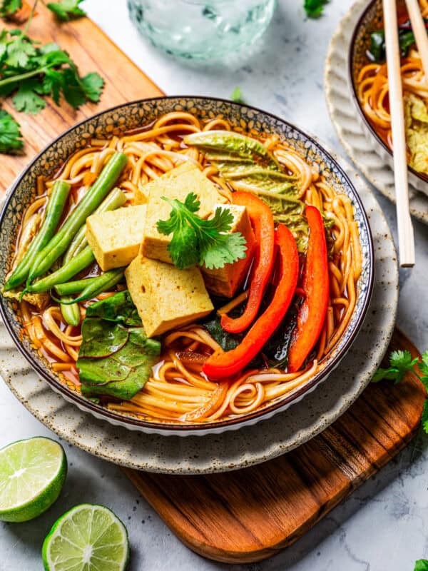 Overhead view of a bowl of noodles and broth topped with Chinese hot pot ingredients on a wooden board.