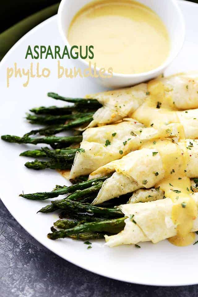 Asparagus phyllo bundles served on a platter with a small bowl of dipping sauce.