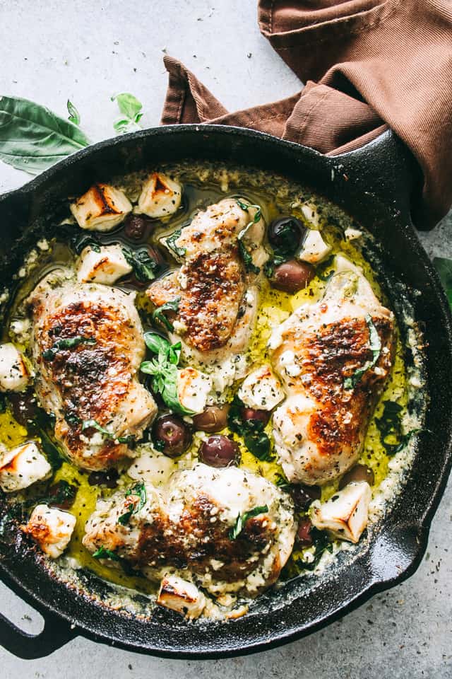 Baked pesto chicken thighs in a sauce with feta cheese, basil pesto, and olives.