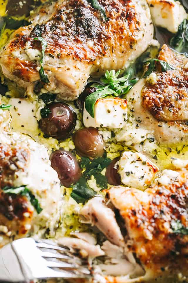 Close-up photo of chicken pieces in a sauce with olives, feta cheese, and basil pesto.