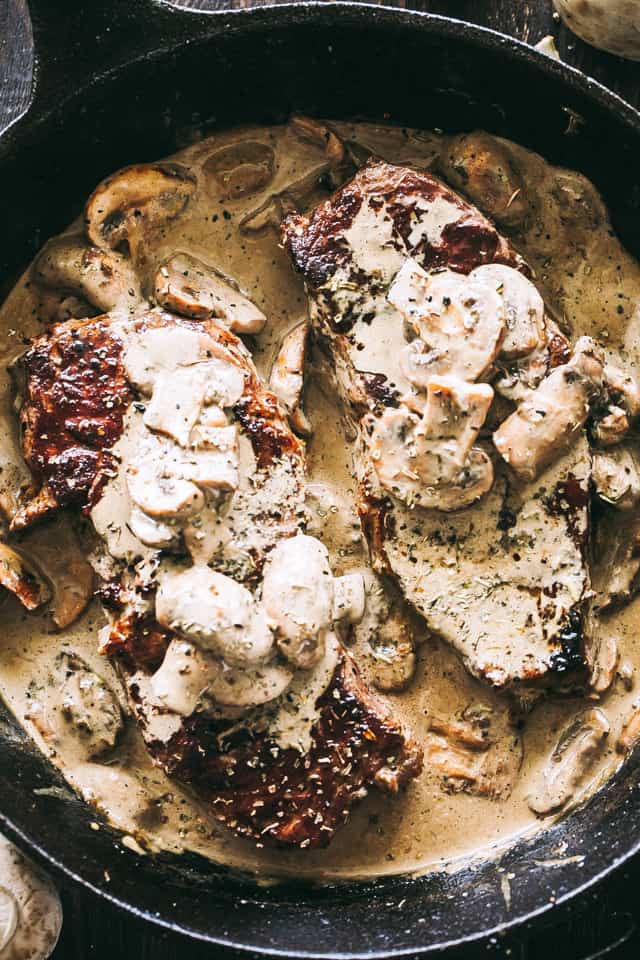 Two sirloin steaks in a skillet are topped with mushrooms and cream sauce.