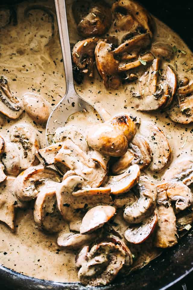 Close up of a spoon stirring through a mushroom sauce in a skillet.