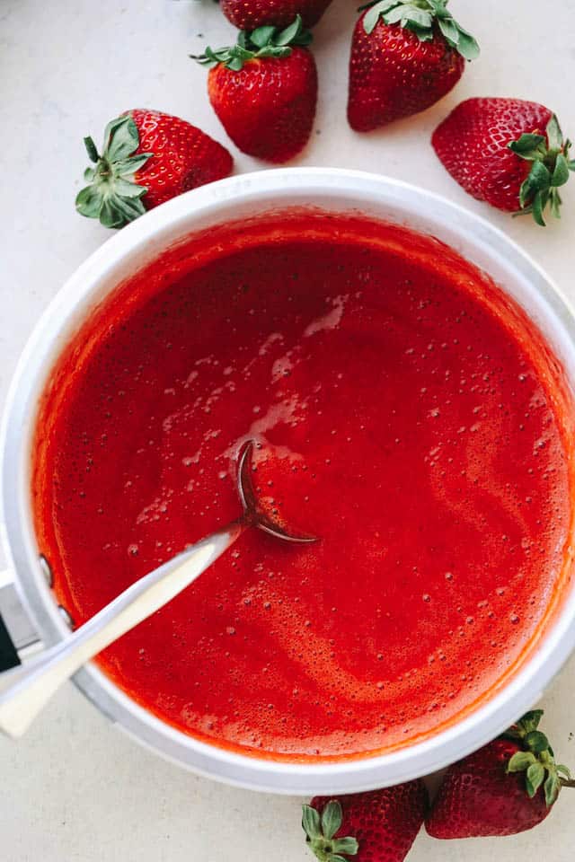 Strawberry Sauce in a saucepan with a spoon mixing through it.