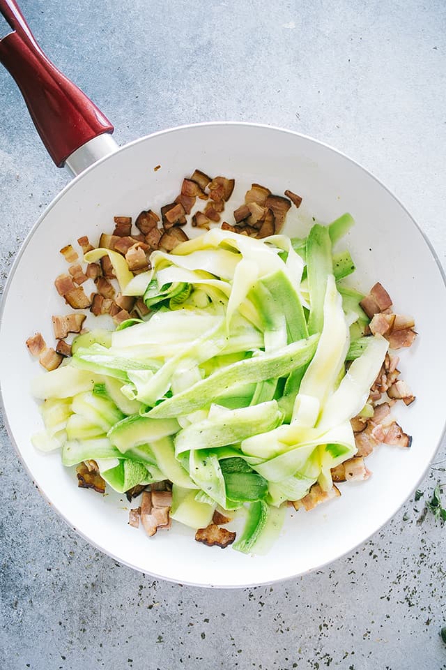 Frying pancetta and zucchini noodles in a pan.