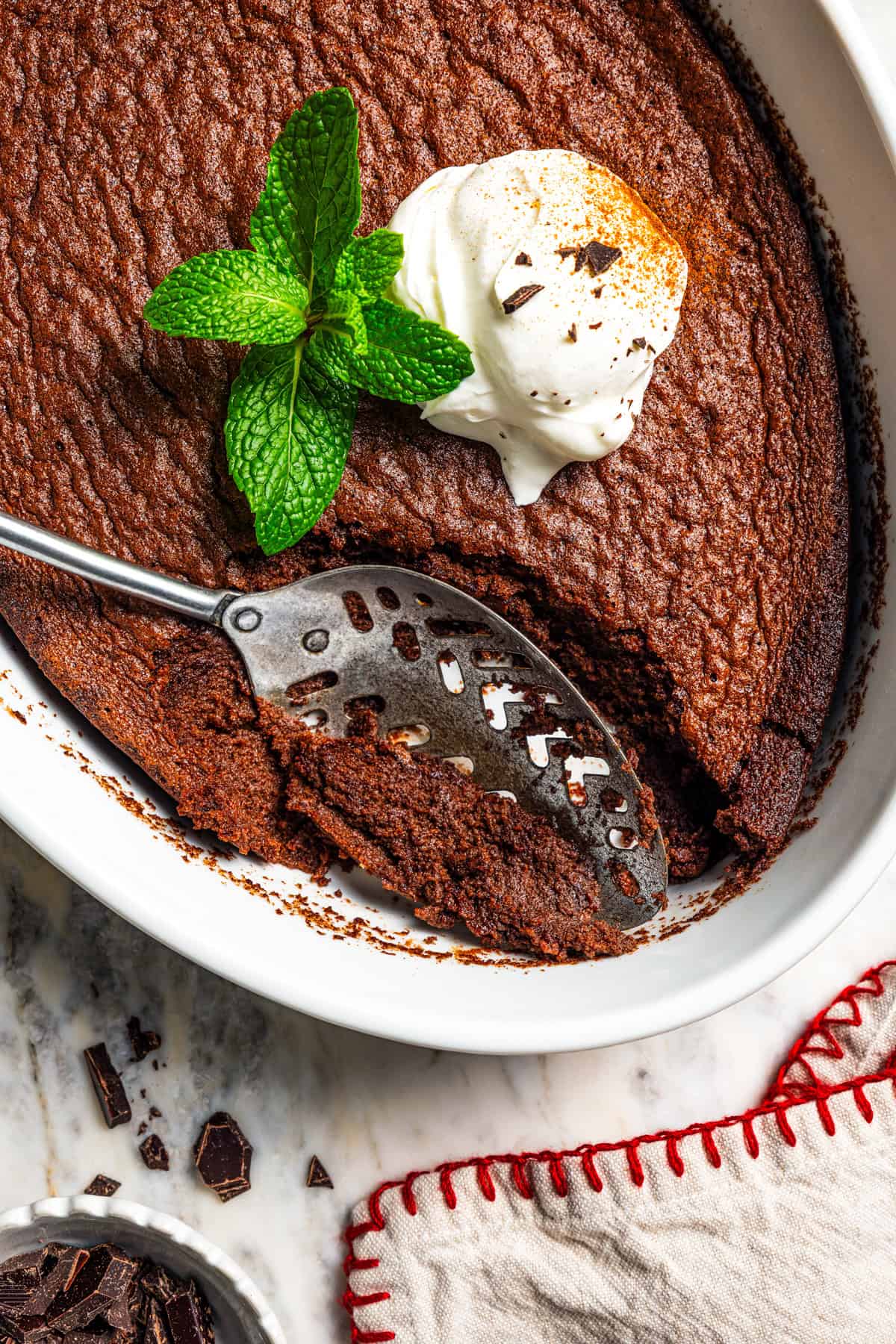 Chocolate fudge cake garnished with whipped cream and mint leaves, with a spoon in an oval baking dish.