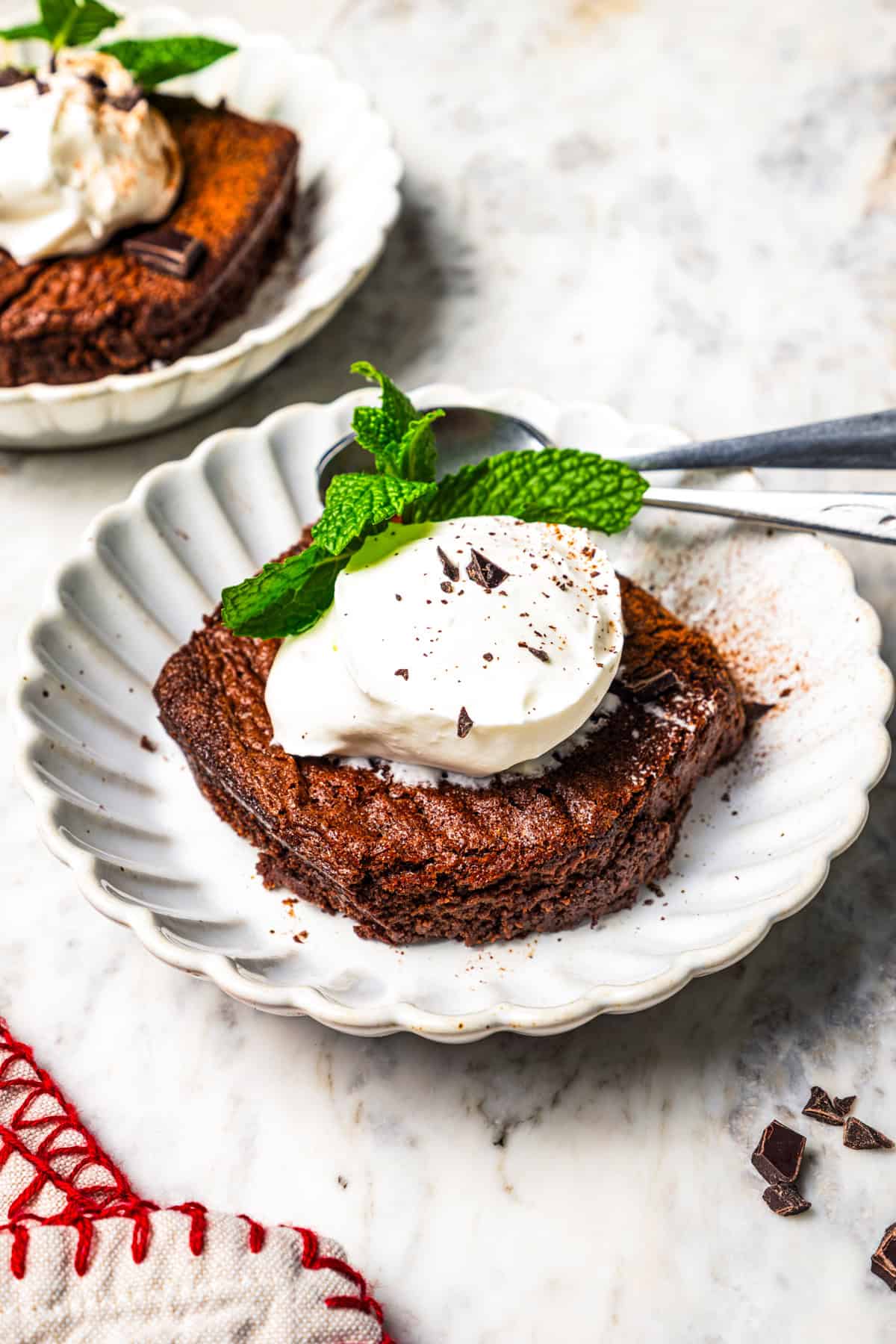 A serving of chocolate fudge cake topped with a dollop of whipped cream, garnished with mint leaves on a plate.