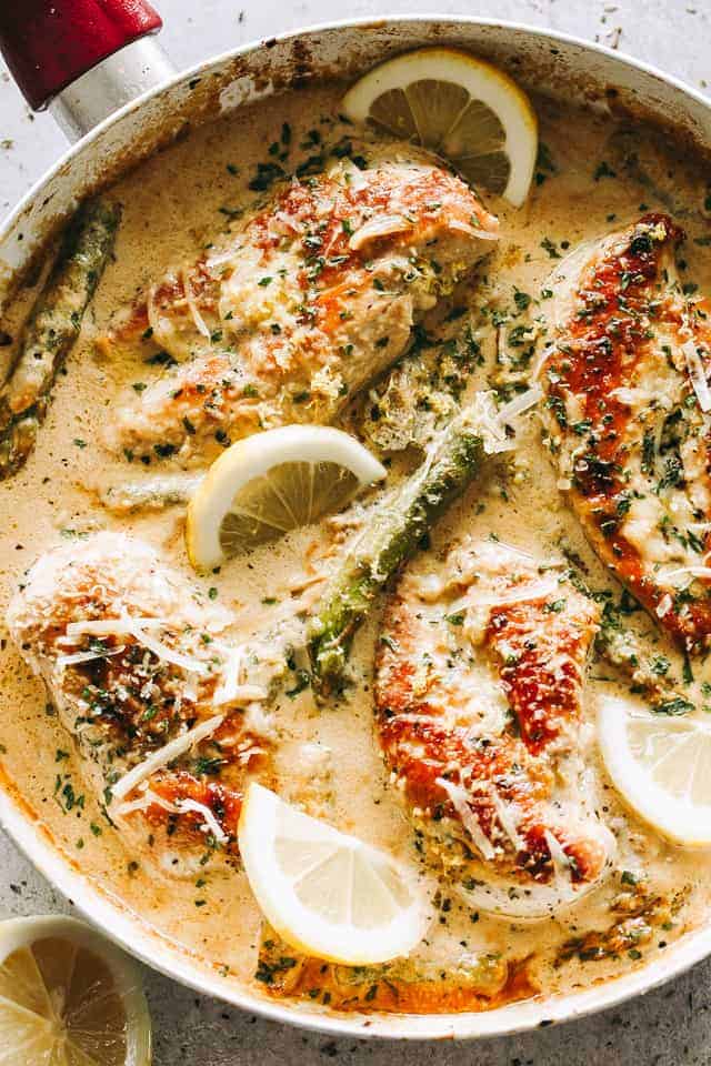 Overhead photo of Creamy Lemon Chicken breasts in a skillet with asparagus, lemon slices, and a sprinkle of parmesan cheese.