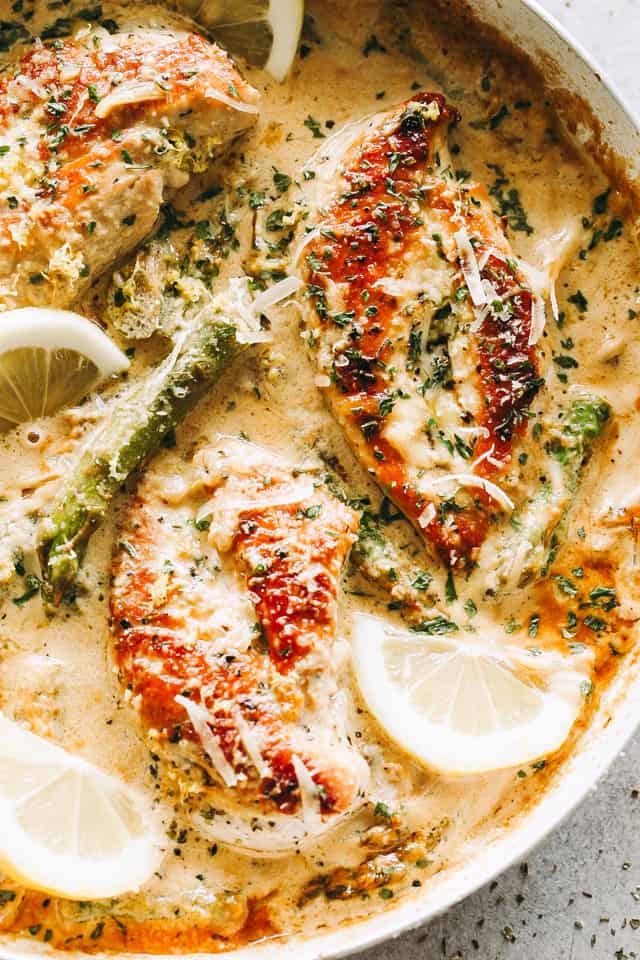 Close-up shot of Creamy Lemon Chicken in a skillet with asparagus, lemon slices, and a sprinkle of parmesan cheese.