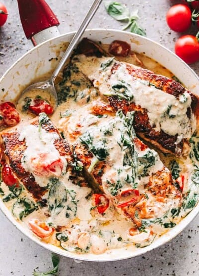 Overhead image of a skillet with three salmon fillets in a cream sauce mixed with baby spinach and cherry tomatoes.