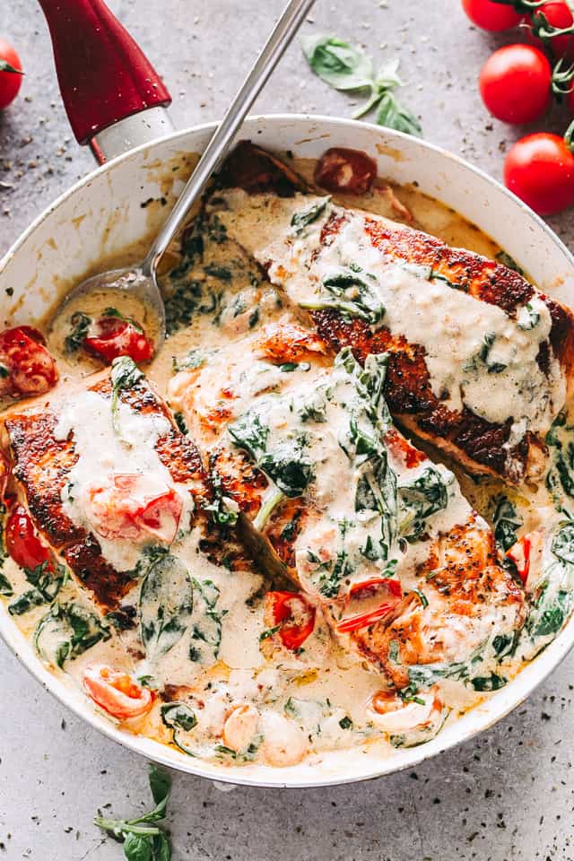 Overhead image of a skillet with three salmon fillets in a cream sauce mixed with baby spinach and cherry tomatoes.