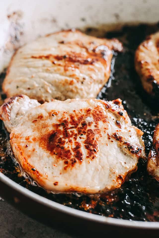 Close up of pork chops searing in a skillet. 