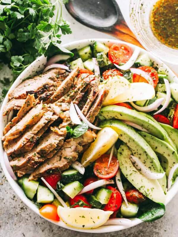 A white plate with sliced steak, diced cucumbers, tomatoes, avocado, cheese, and onions.