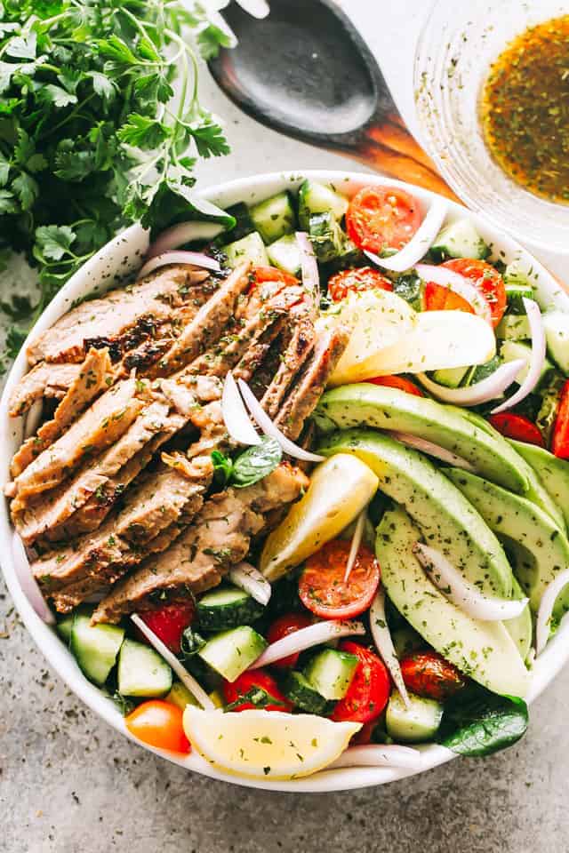 A white plate with sliced steak, diced cucumbers, tomatoes, avocado, cheese, and onions.