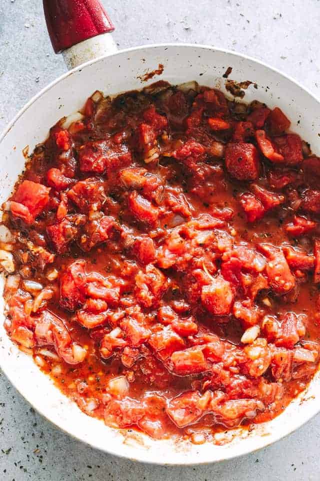 Adding tomatoes, tomato paste, oregano, basil, half & half, and capers to a skillet with sautéed onions, garlic, and white wine.