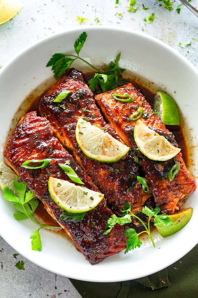 Three Salmon Fillets served on a white plate and garnished with lime slices and green onions.